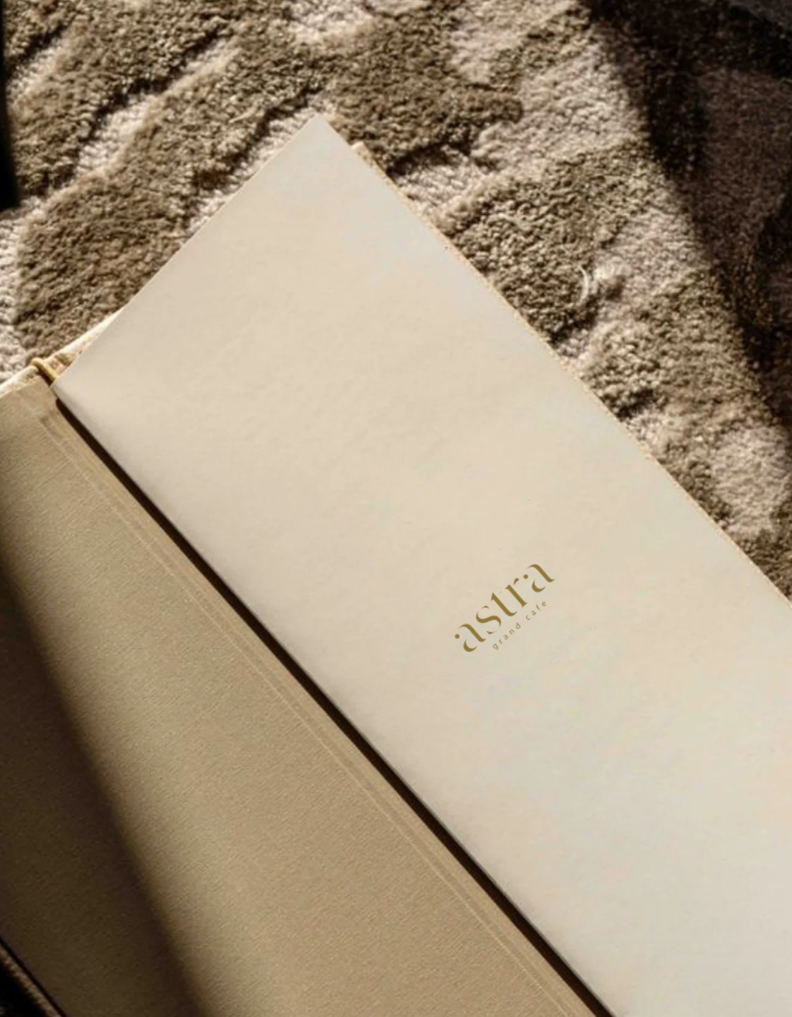 ASTRA cream menu cover with a small gold wordmark on a textured stone surface